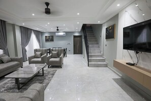 A modern living room with a sofa set, a coffee table, and a TV on a marble wall. - Casa Maria facility, Spacious Home Sleeps 4–8, Perfect for Families & Groups (Kumasi)
