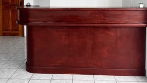 A reception desk with a painting of two figures on a boat, a wooden door, and a white tiled floor. - La Isla Del Descanso (Puerto Villamil)