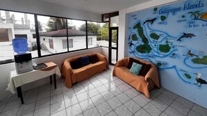 A room with a large window, a map of the Galápagos Islands on the wall, a sofa, a small table with a water dispenser, and a blue water container. - La Isla Del Descanso (Puerto Villamil)