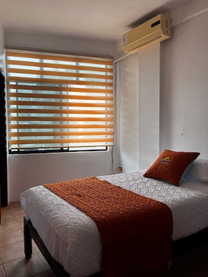 A bedroom with a bed, an air conditioning unit, a window with blinds, and a pillow. - La Isla Del Descanso  (Puerto Villamil)