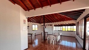 A spacious indoor area with a high wooden ceiling, tiled floor, and large windows offering views of the outdoors. - La Isla Del Descanso (Puerto Villamil)