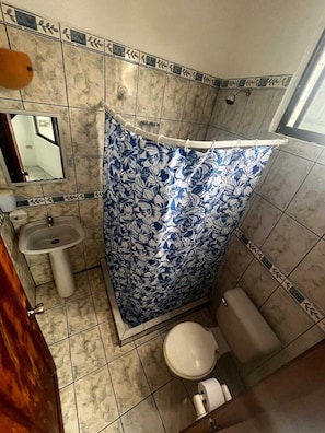 A small bathroom with a shower curtain, sink, toilet, and a mirror. - La Isla Del Descanso  (Puerto Villamil)