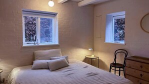 Une chambre à coucher avec un lit, deux fenêtres, une table de chevet, une chaise et une commode.