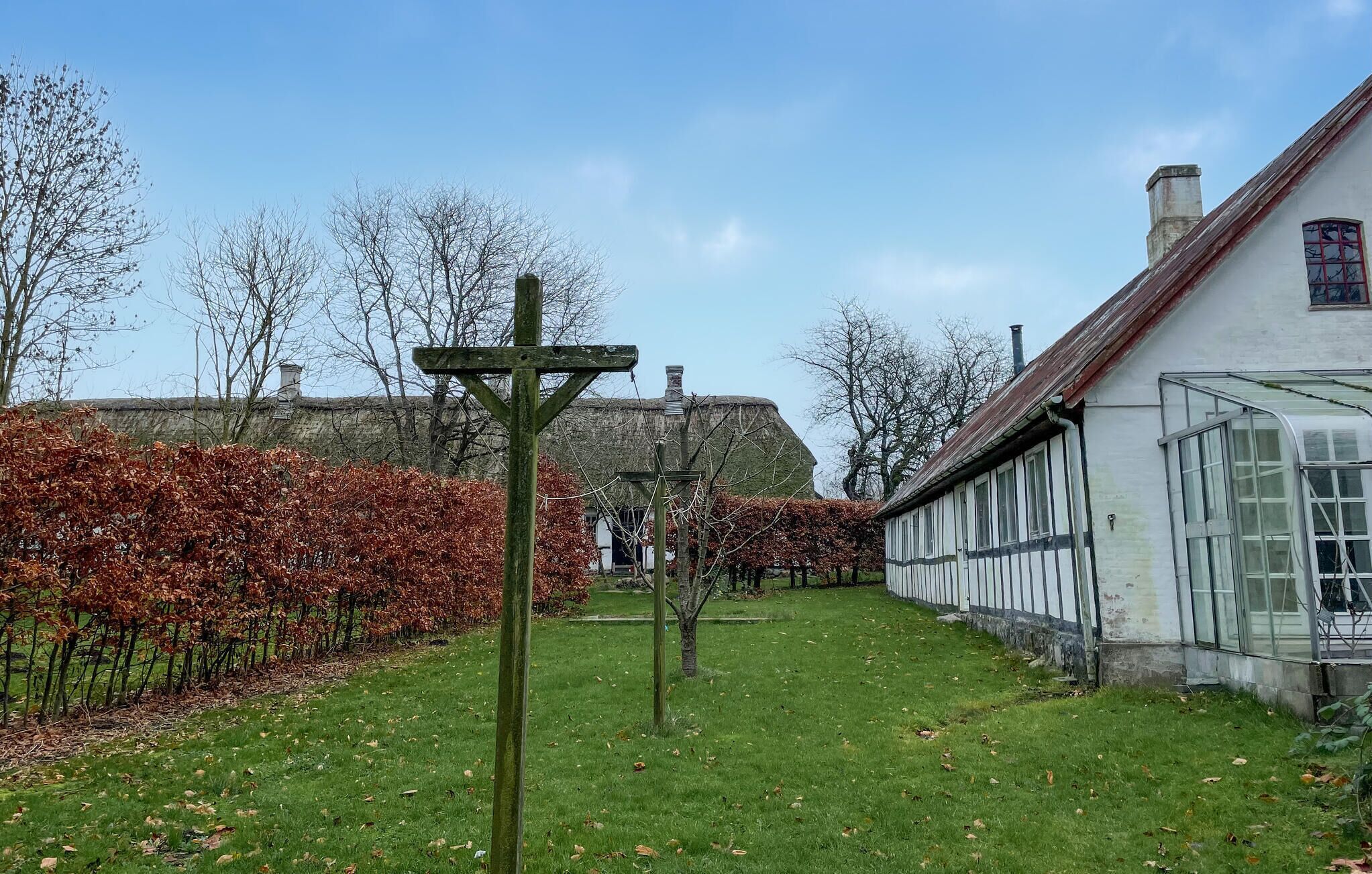 A traditional building with a thatched roof, a greenhouse, and a well-maintained garden with a wooden signpost.