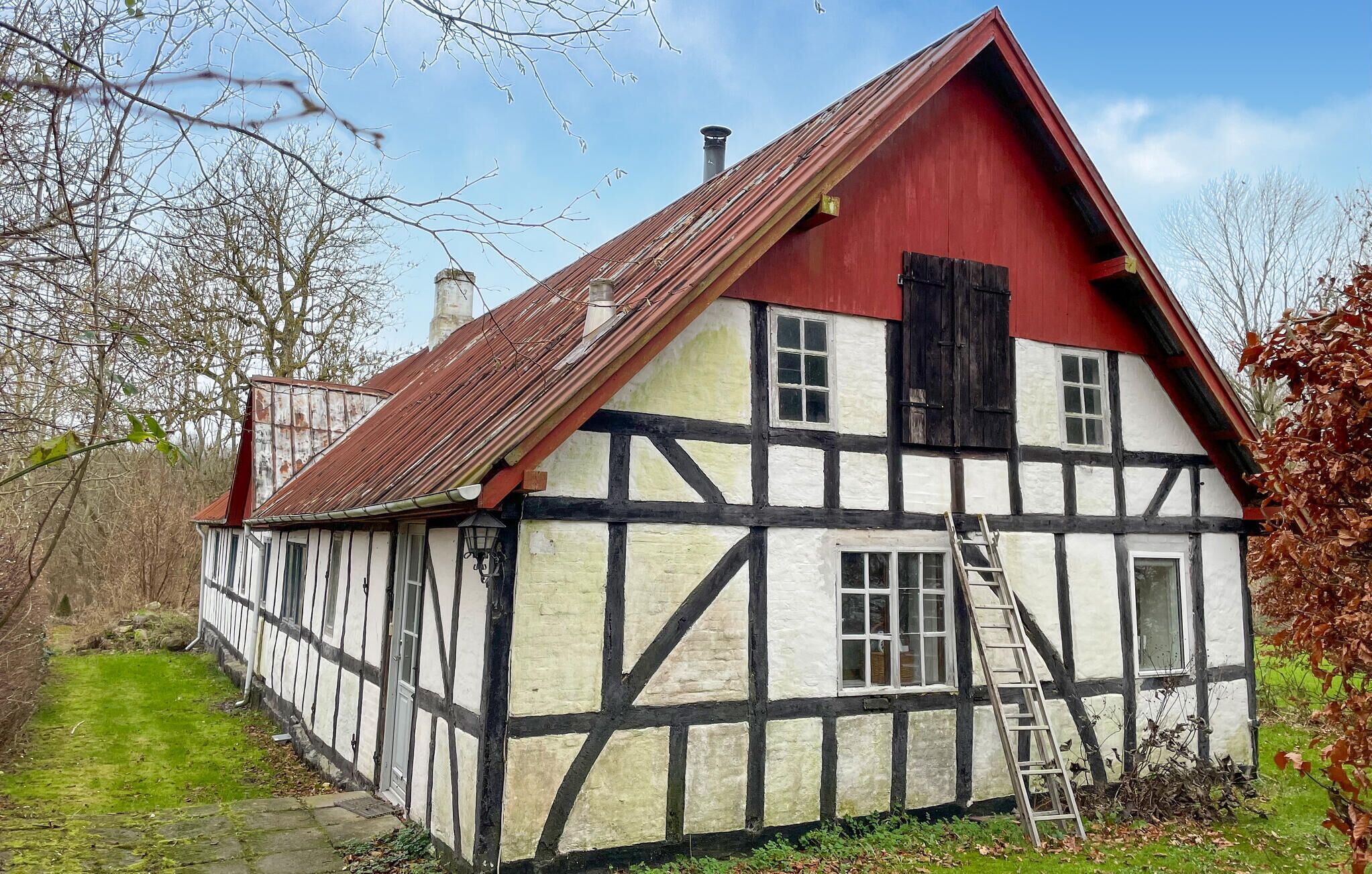A traditional half-timbered house with a steep red roof, a visible chimney, and a ladder leaning against the side.