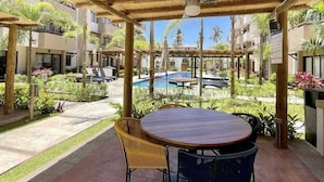 An outdoor patio with a round table and chairs, surrounded by greenery and a pool. - Apartment in private condominium near the sea (Mazatlán)