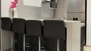 A modern kitchen with white and dark grey cabinetry, a stainless steel refrigerator, and three black bar stools. - Apartment in private condominium near the sea (Mazatlán)