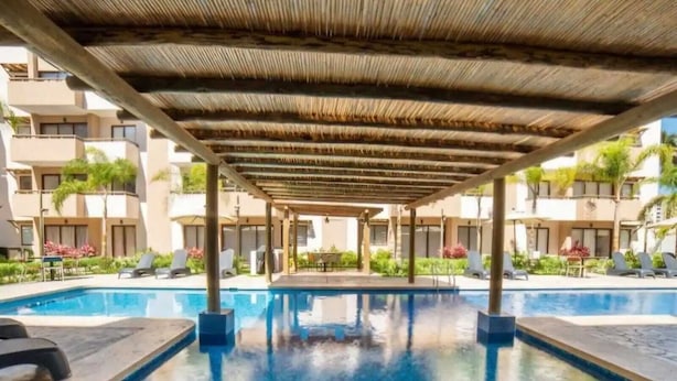 A swimming pool with a covered area, lounge chairs, and a building with balconies in the background. - Apartment in private condominium near the sea (Mazatlán)