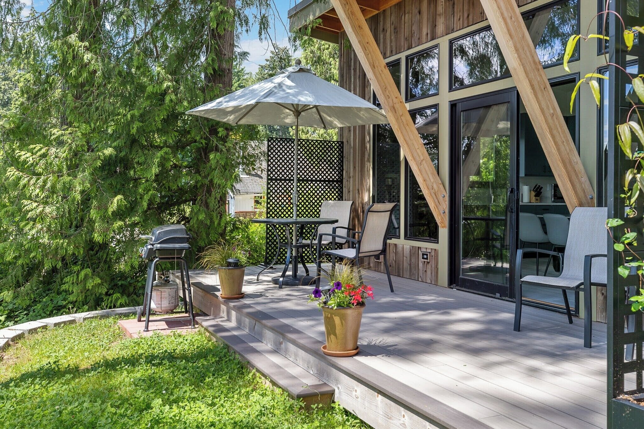 Une terrasse en bois avec des meubles d’extérieur, un barbecue et des plantes en pot.