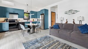 Una cocina moderna con armarios azules, una zona de comedor con una mesa redonda y un sofá gris con cojines azules.