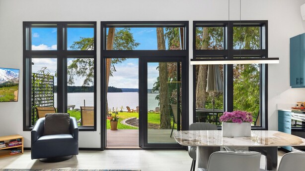 Una cocina moderna con amplios ventanales, una mesa de comedor y vistas a un lago y jardín.