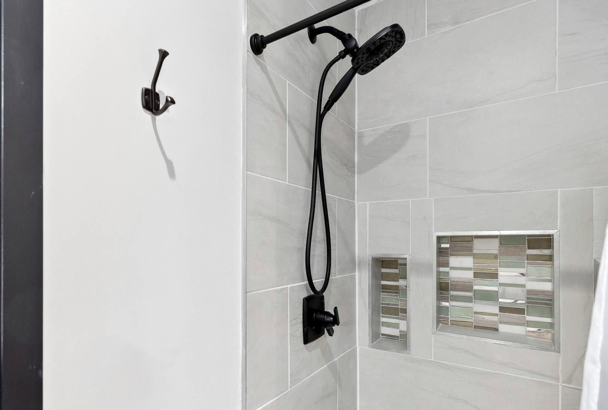 Een douchegedeelte met een handdouche en bediening aan de muur.