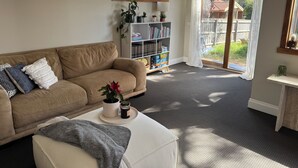 Een woonkamer met een beige bank, een witte salontafel en een boekenkast.