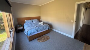 Een slaapkamer met een houten bed, een klein nachtkastje, een raam en een deur naar een andere kamer.