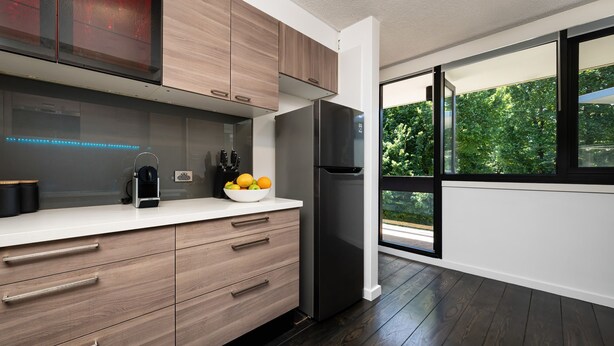 Una cucina moderna con mobili in legno, un frigorifero nero e una ciotola di frutta sul piano di lavoro.
