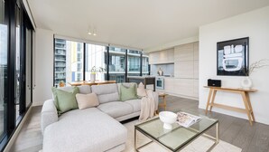 Una sala de estar moderna con un sofá modular, una mesa de centro de vidrio y una cocina al fondo.
