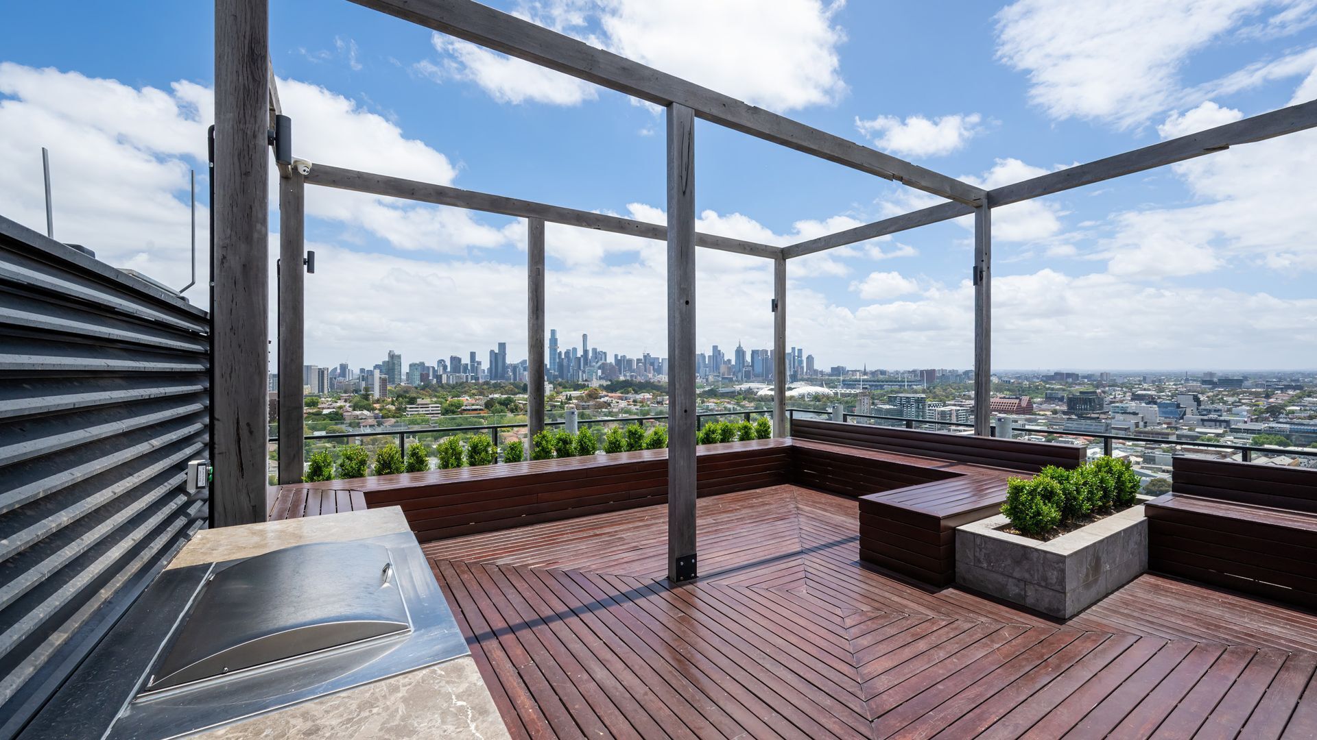 Une terrasse sur le toit offrant une vue panoramique sur la ville, avec un sol en bois et des espaces aménagés pour s’asseoir.