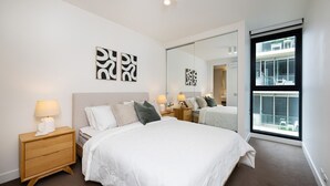 Un dormitorio moderno con una cama grande, mesitas de noche, un espejo y obras de arte en las paredes.