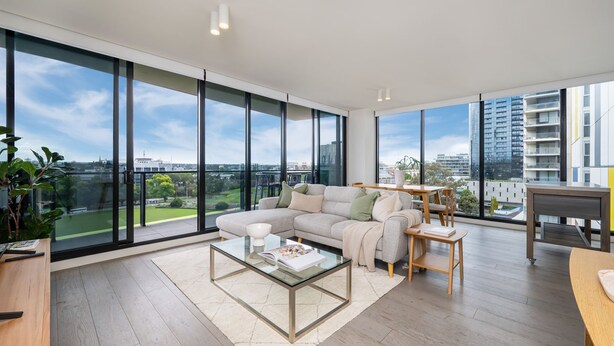 Una sala de estar moderna con ventanas amplias, un sofá modular, una mesa de centro de vidrio y vistas de la ciudad.