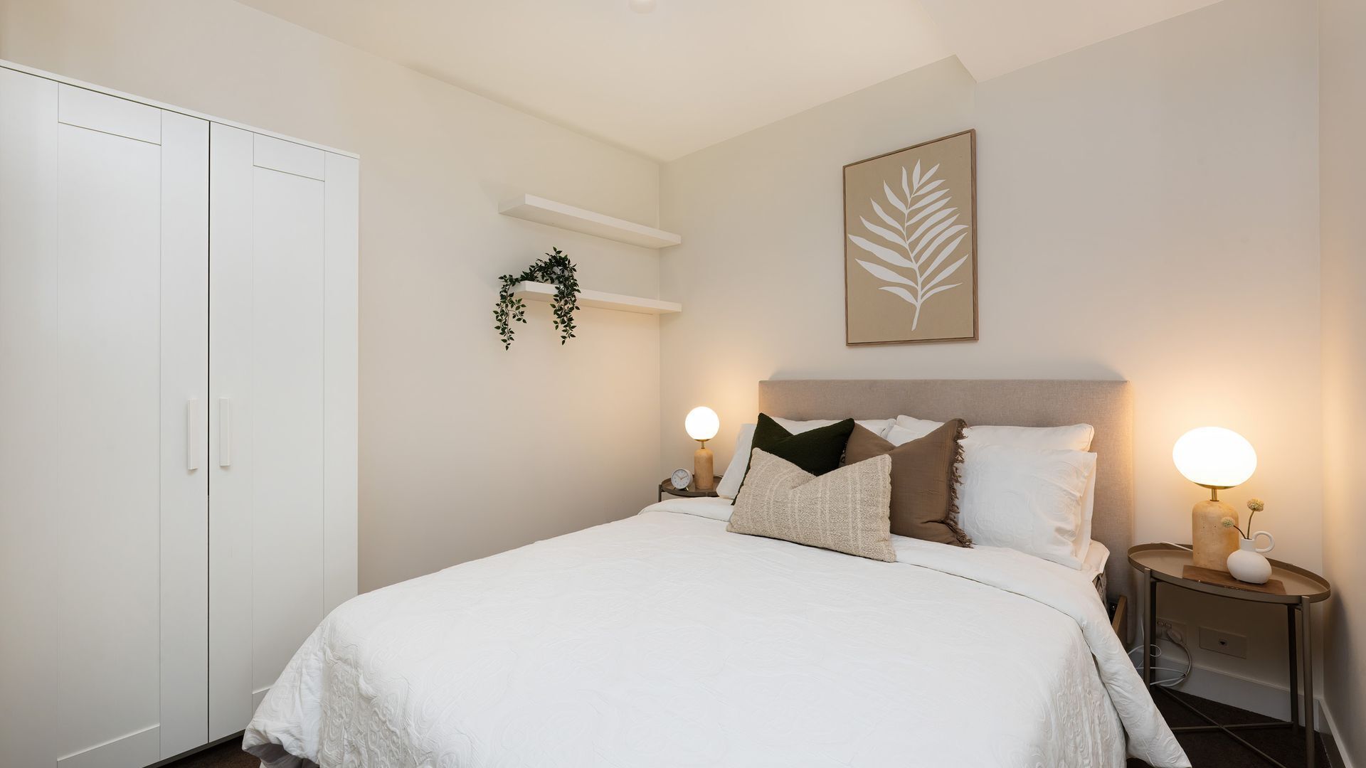 Une chambre à coucher comprenant un lit, des tables de chevet, une armoire, une étagère fixée au mur et une œuvre d’art décorative.