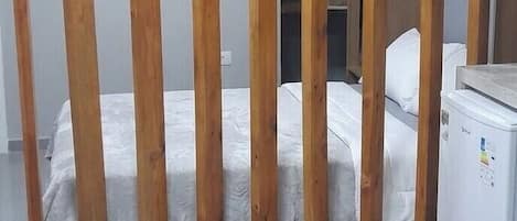 A room with a bed, a white chair, a wooden partition, and a white refrigerator.