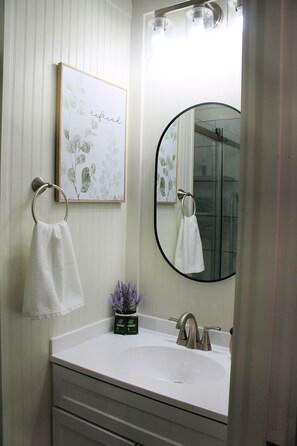 A bathroom with a white sink, a mirror, and a towel ring. - Charming tiny house in Russellville (Russellville)