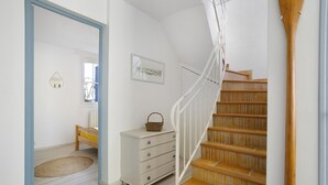 Un escalier avec des marches en bois et une rampe blanche, une commode blanche avec des tiroirs, un petit tapis et un tableau encadré accroché au mur.