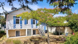 Une maison à deux étages dotée d’un balcon, d’une façade en pierre et d’un jardin agrémenté d’un arbre et de mobilier d’extérieur.