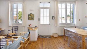Une pièce avec un plancher en bois, une table à manger avec des chaises, une fenêtre avec des rideaux et une porte.