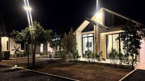 A modern house with a spacious garden, large windows, and a well-lit exterior at night.