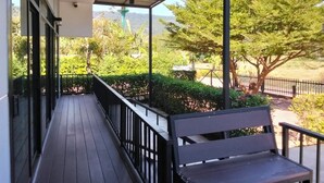 A covered outdoor area with a wooden deck, a bench, and a view of greenery and hills in the background.