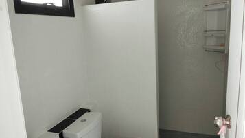 A small, compact bathroom with a toilet, a shower stall, and a white sink.
