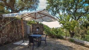 An outdoor patio with stone walls, a stone oven, and a table with chairs under a large umbrella. - 2 bedroom stunning home in Perdifumo (Perdifumo)