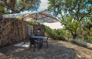 An outdoor patio with stone walls, a stone oven, and a table with chairs under a large umbrella.