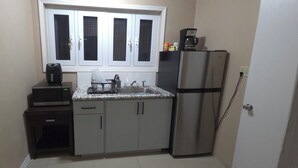 Eine kleine Küche mit Mikrowelle, Kaffeemaschine, Kühlschrank und einem Fenster über der Spüle.