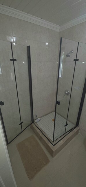A glass-enclosed shower with a tiled floor and a small rug. - Golden Haven –Comfort in the Heart of Paradise in The Bahamas - entire apartment (Nassau)