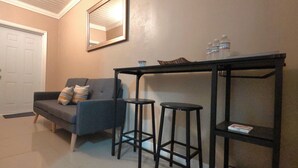 Ein Flur mit einem grauen Sofa, zwei schwarzen Barhocker, einem kleinen Tisch mit Wasserflaschen und einem Spiegel an der Wand.