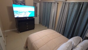 Ein Schlafzimmer mit einem Bett, einem Fernseher auf einer Kommode und Vorhängen.