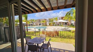 A view of a pool area with lounge chairs and a table, surrounded by palm trees and modern buildings.