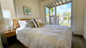 A bedroom with a bed, a nightstand, a window, and a view of the outside.