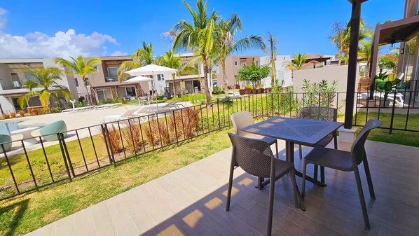 A patio area with a table and chairs, a pool, and surrounding buildings.