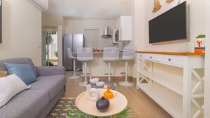 Un soggiorno moderno con un divano grigio, un tavolino da caffè con oggetti decorativi e un'area pranzo con sedie bianche e una televisione.