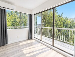 A room with large windows, a balcony with a white railing, and a wooden floor. - Modern 1 Bedroom Suite with Parking (North Vancouver)
