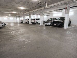 A parking garage with multiple rows of parked cars and concrete pillars. - Modern 1 Bedroom Suite with Parking (North Vancouver)