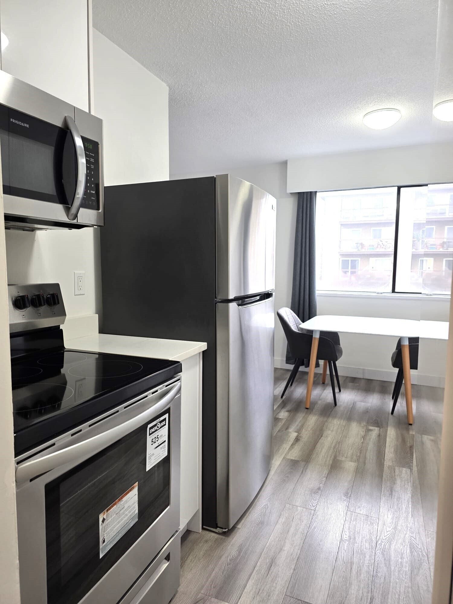 Cocina moderna con horno integrado, microondas y refrigerador de acero inoxidable. Hay una mesa de comedor con sillas y una ventana que ofrece vistas al exterior.