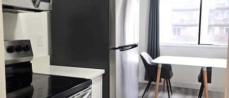 Cocina moderna con horno integrado, microondas y refrigerador de acero inoxidable. Hay una mesa de comedor con sillas y una ventana que ofrece vistas al exterior.