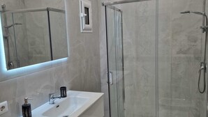 Un baño moderno con ducha de vidrio, tocador blanco con un espejo grande y un inodoro.