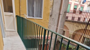 Un pasillo estrecho con suelo de baldosas, barandilla de metal verde y una ventana con marco blanco.