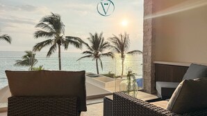 A balcony with wicker furniture, a glass barrier, and a view of the sea and palm trees.