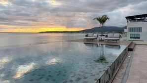 An infinity pool with a view of the sea and mountains at sunset.